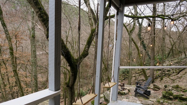 Una terraza de madera con un columpio, un banco y una lámpara colgante.