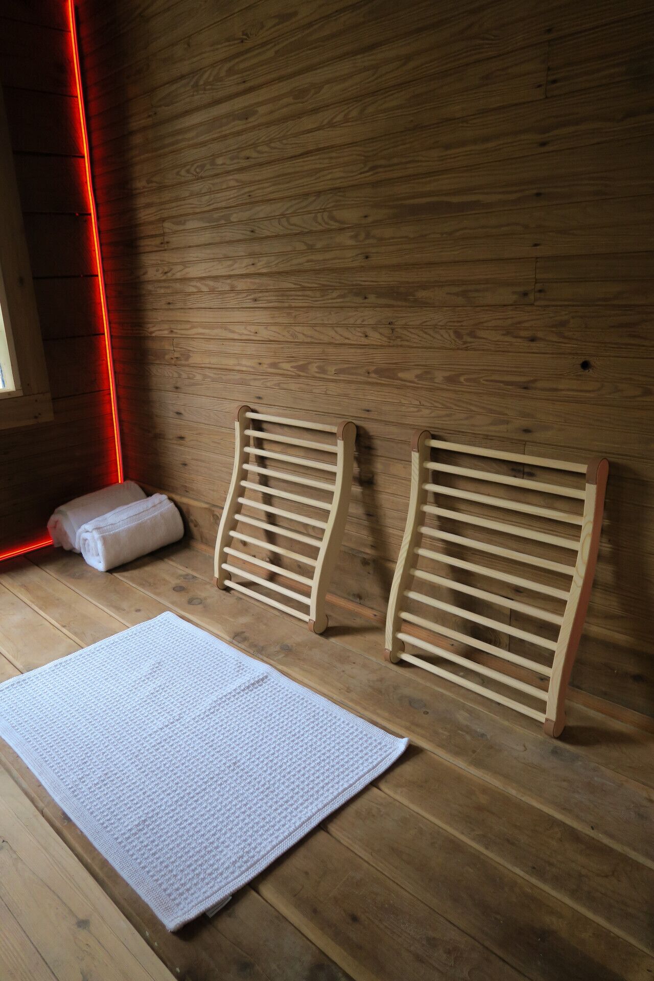 Sala de sauna com paredes e banco de madeira, uma toalha e um tapete.