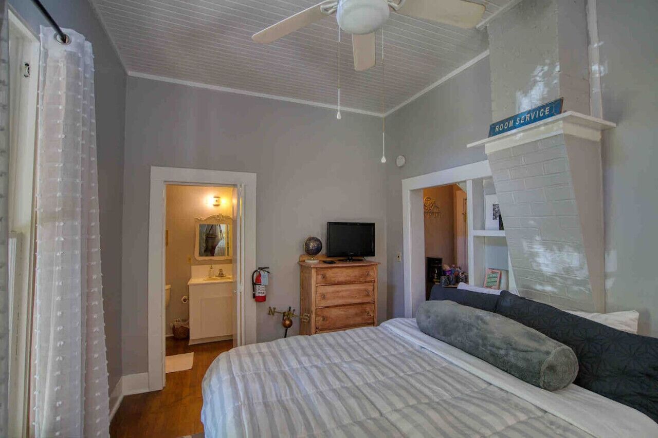 A bedroom with a bed, a ceiling fan, a television on a wooden dresser, and a sign indicating room service.