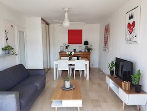 En moderne stue med en grå sofa, et træbord, et spiseområde med en rød accentvæg og et fjernsyn på et hvidt skab.