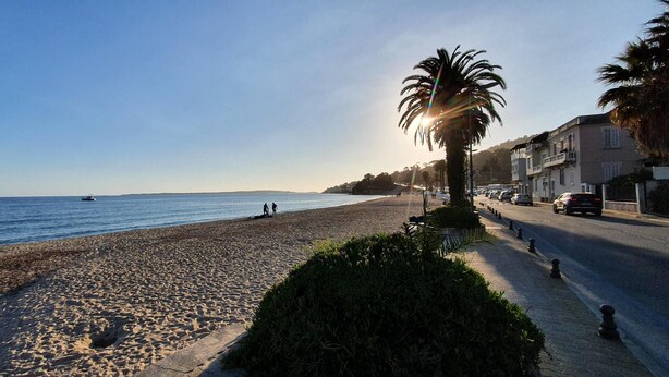 A beach with a clear sky, a few people, and a road with cars. - Charming T2 48m² Balcony Sea View 4 sleeps 2min from the Beach (Vallauris)