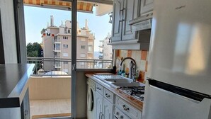 A compact kitchen with a built-in oven, a stainless steel refrigerator, and a view of the city through a sliding glass door. - Charming T2 48m² Balcony Sea View 4 sleeps 2min from the Beach (Vallauris)