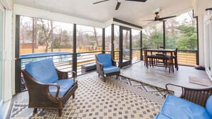 Une terrasse couverte, aménagée avec des meubles en osier, un ventilateur de plafond et offrant une vue sur une piscine et des arbres.