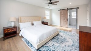 Une chambre avec un grand lit, un ventilateur de plafond, une table de chevet, une lampe, une porte coulissante et une vue sur l’extérieur.