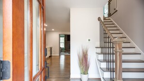 Un hall d’entrée spacieux avec un plancher en bois, un escalier doté d’une rampe en bois et une plante en pot.