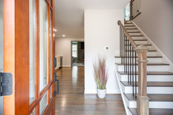 Un hall d’entrée spacieux avec un plancher en bois, un escalier doté d’une rampe en bois et une plante en pot.
