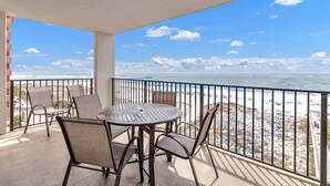 Un balcon avec une table et des chaises, donnant sur une plage sous un ciel dégagé.