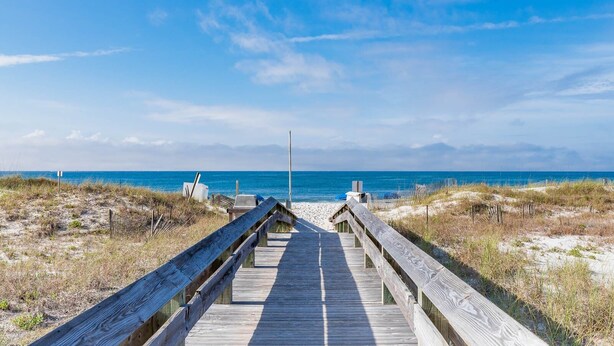Une promenade en bois qui mène à une plage offrant une vue dégagée sur l’océan.
