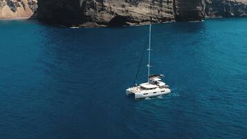 Un velero anclado cerca de una costa rocosa con un acantilado destacado y un pequeño edificio en la cima.