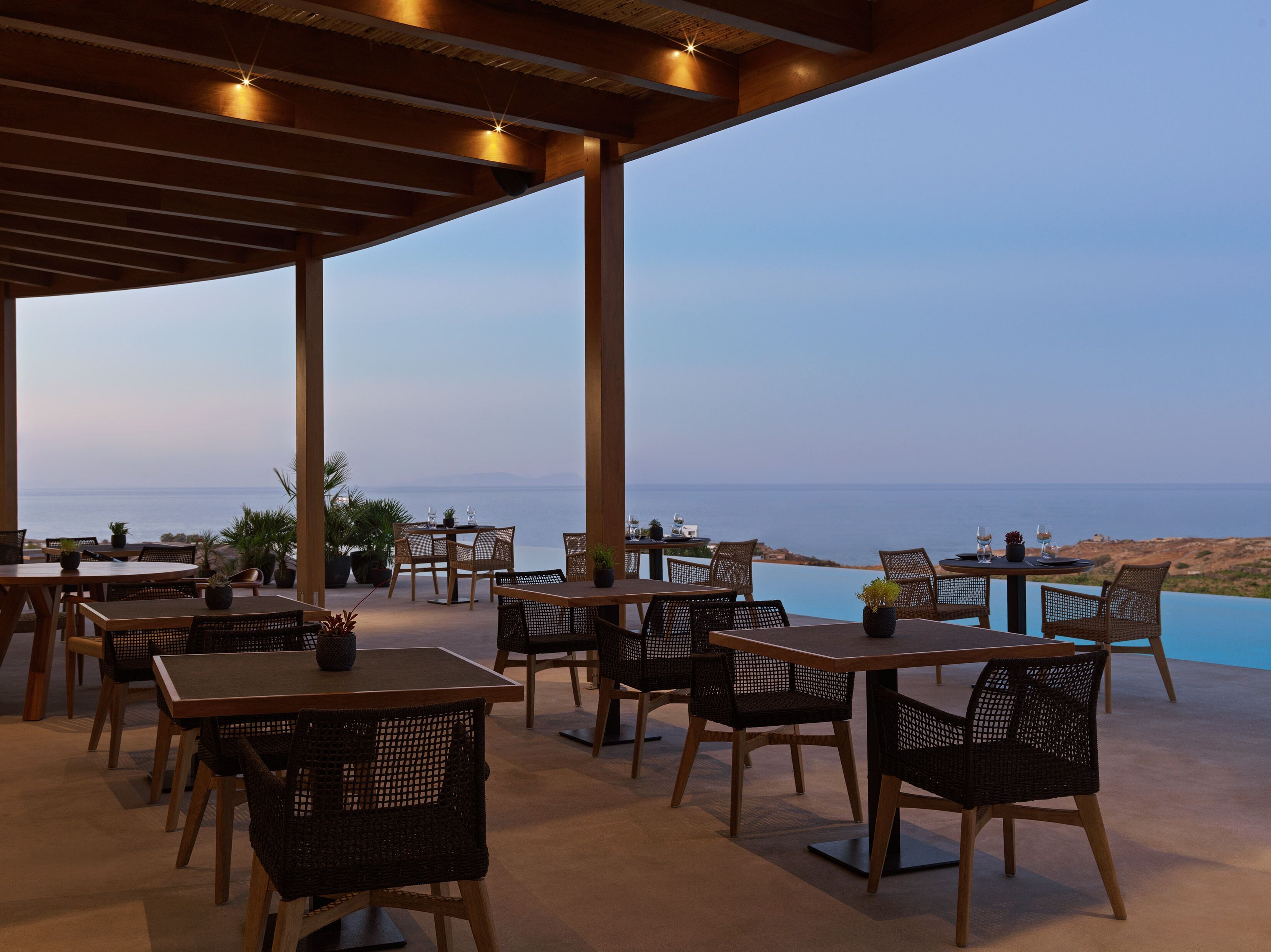 An outdoor dining area with tables and chairs, overlooking a body of water.