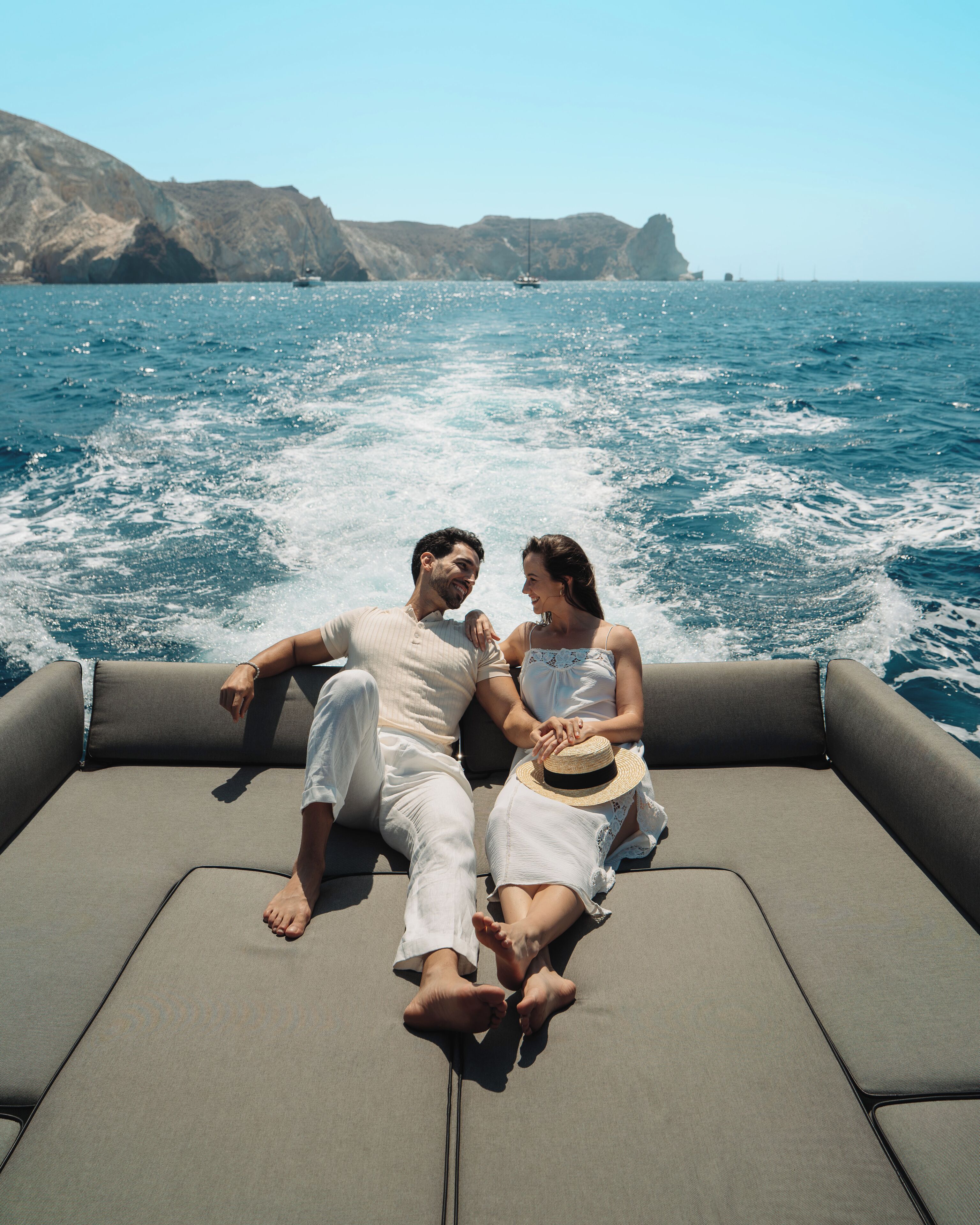 Un couple est à bord d’un bateau, avec une vue sur la mer et les falaises.