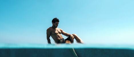 A man sitting on the edge of a pool with a clear blue sky in the background.