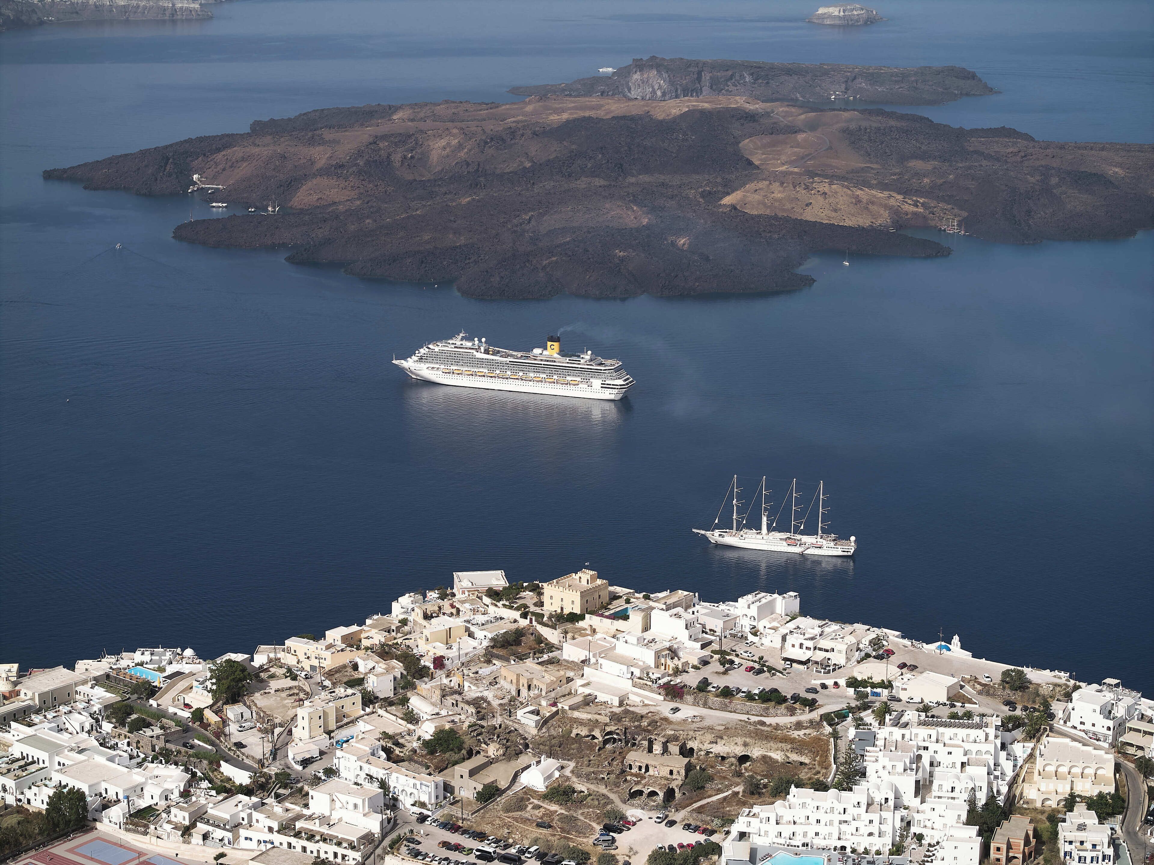 Une ville côtière où un grand navire de croisière est amarré près d’un plus petit voilier.