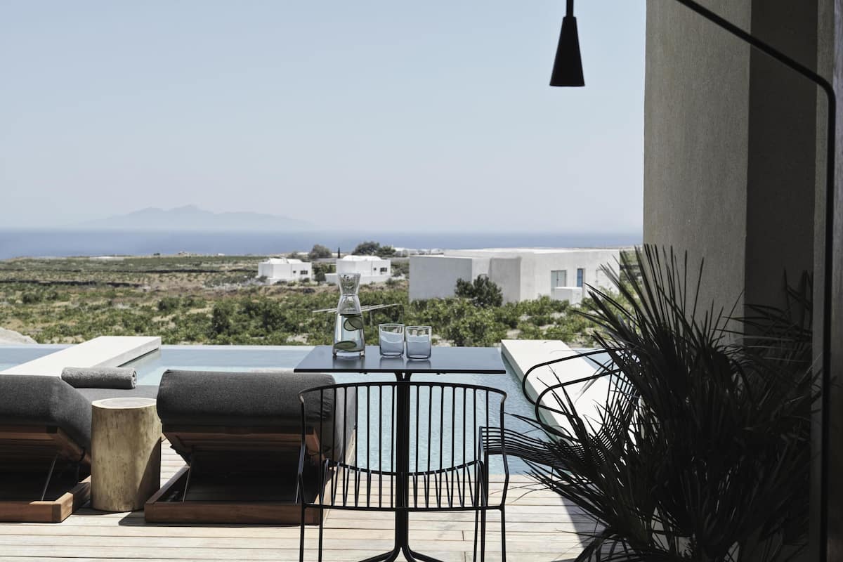 Eine Terrasse mit Tisch, Stühlen und einer Lampe. Im Hintergrund sind Gebäude und eine Landschaft zu sehen.