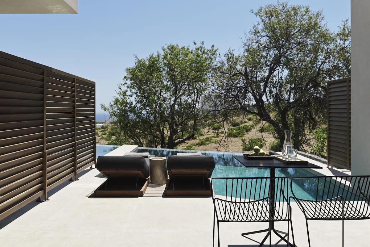 Ein moderner Poolbereich im Freien mit Liegestühlen und einem Tisch, umgeben von Bäumen und Blick auf die Landschaft.