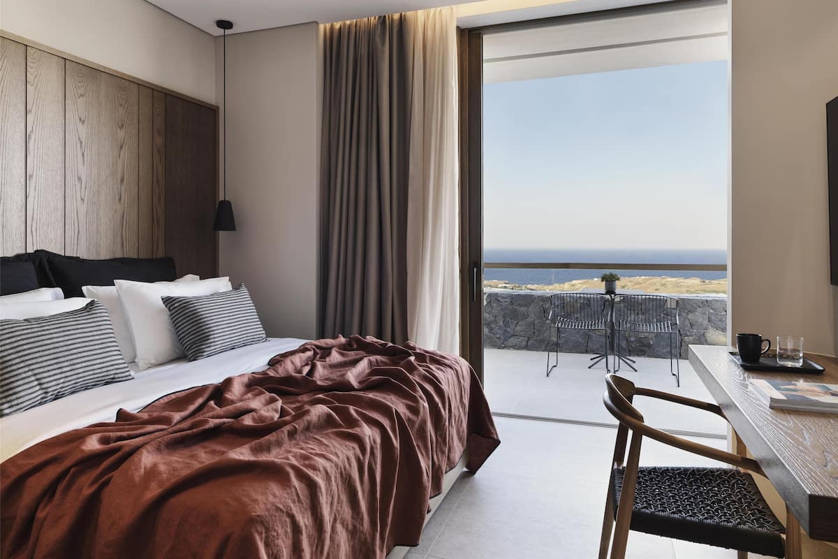 Ein Schlafzimmer mit einem großen Bett, Meerblick, einem Balkon mit Tisch und Stühlen sowie einer Holzwand.