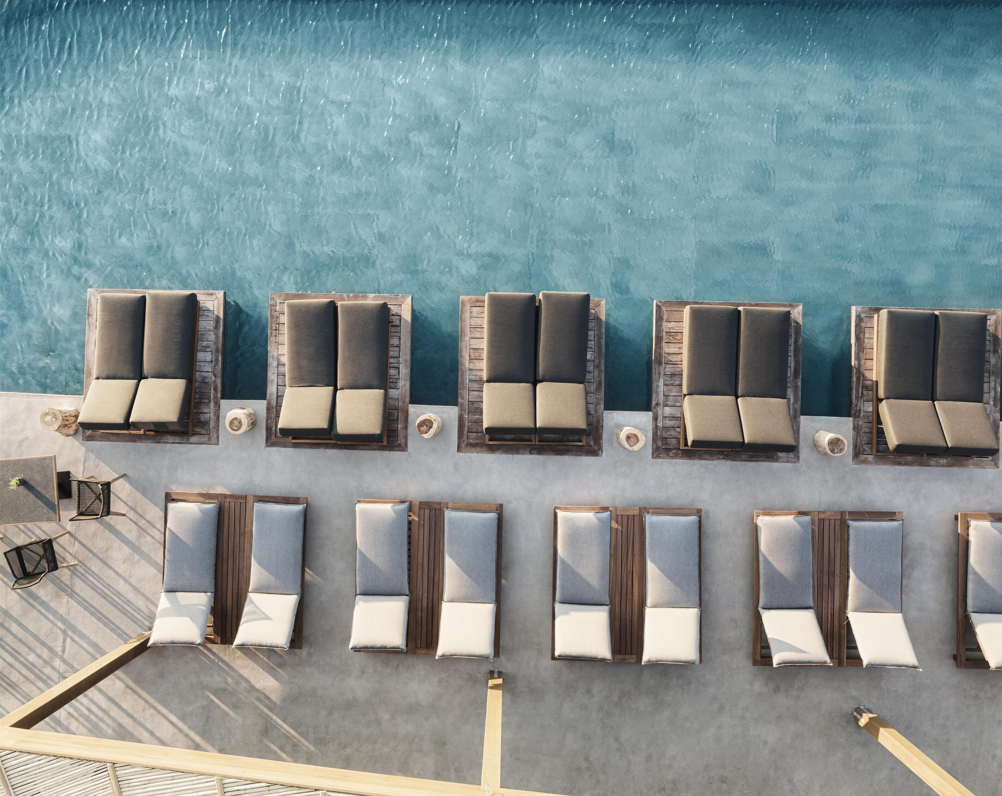 An aerial view of a poolside area with multiple lounge chairs and a small table, surrounded by a concrete deck.