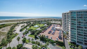 A high-rise hotel with a parking lot, a fountain, and a view of the beach and ocean.