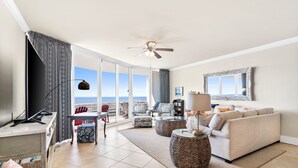 A spacious living room with a balcony, a ceiling fan, a sofa, a coffee table, and a TV.