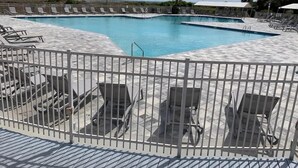 Una piscina con varias pistas, rodeada de tumbonas y una zona de terraza delimitada.
