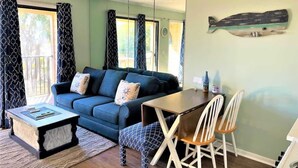 Una sala de estar con un sofá azul, una mesa de centro de madera y una mesa de comedor con sillas.
