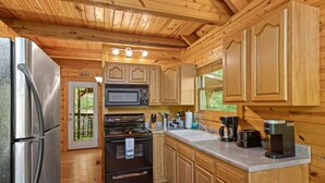 A wooden cabin kitchen with a refrigerator, stove, microwave, and coffee maker. - Beary Secluded- No Pet Fee, Hot Tub, Firepit, WiFi (Slade)