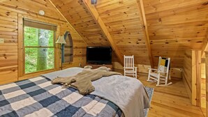 A cozy attic bedroom with a wooden ceiling, a bed with a checkered blanket, a television, and two rocking chairs. - Beary Secluded- No Pet Fee, Hot Tub, Firepit, WiFi (Slade)