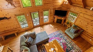 A cozy cabin with a loft-style ceiling, a fireplace, a television, and a large window overlooking greenery. - Beary Secluded- No Pet Fee, Hot Tub, Firepit, WiFi (Slade)