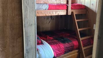 A bunk bed with a ladder, wooden walls, and a window with curtains.