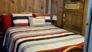 A wooden cabin-style bedroom with a bed, pillows, and a shelf with decorative ducks. - Cute Family Cabin at Lakeview by Sue  (Appleton City)