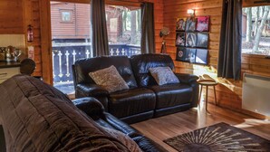 A cozy cabin interior with a leather sofa, a small side table, and a bookshelf filled with books and decorations. - Kenwick Lodge - UK37416 (Kenwick, near Louth)