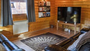 A cozy cabin interior with a wooden interior, a large flat-screen TV, a leather sofa, and a rug. - Kenwick Lodge - UK37416 (Kenwick, near Louth)