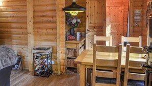 A wooden cabin interior with a dining table, chairs, a hanging light fixture, a small shelf with decorative items, and a wine rack. - Kenwick Lodge - UK37416 (Kenwick, near Louth)
