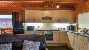 A cozy cabin-style kitchen with wooden cabinets, a black refrigerator, a microwave, and a coffee maker. - Kenwick Lodge - UK37416 (Kenwick, near Louth)