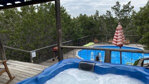 A hot tub with a wooden deck and a pool in the background. - Cozy Cottage with Private pool, Private Hot Tub and Internet (Wimberley)