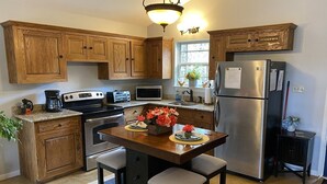 A kitchen with wooden cabinets, a stainless steel refrigerator, a stove, and a microwave. There is a dining table with chairs and a vase of flowers. - Cozy Cottage with Private pool, Private Hot Tub and Internet (Wimberley)