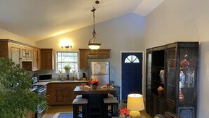 A kitchen with wooden cabinets, a central island with stools, a refrigerator, and a dining table set with flowers. - Cozy Cottage with Private pool, Private Hot Tub and Internet (Wimberley)