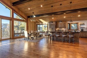 A spacious kitchen with wooden flooring, large windows, and a bar area.