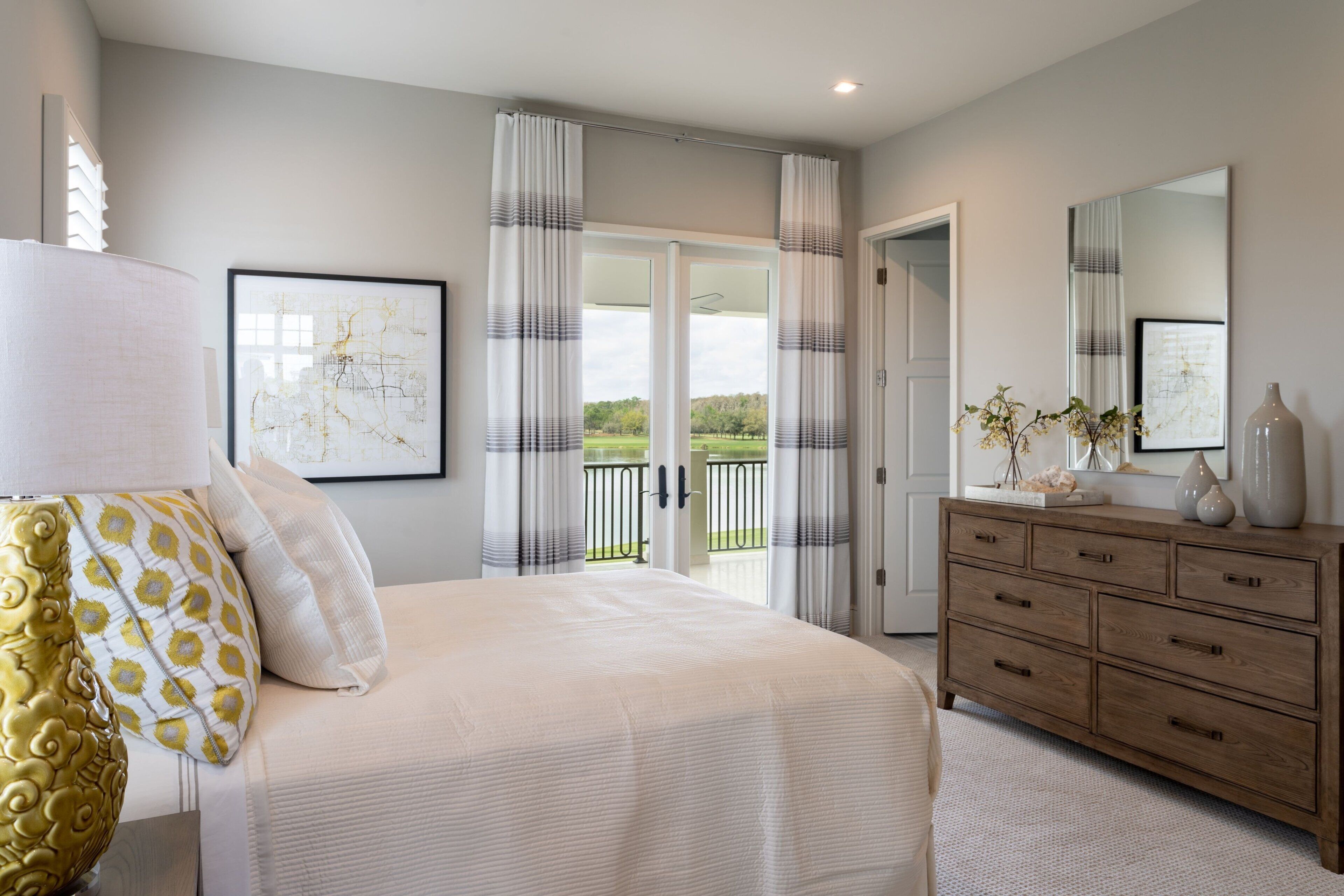 A bedroom with a bed, a dresser, a lamp, and a large window with curtains.