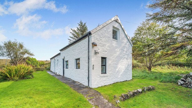 Un bâtiment blanc avec un toit en pente, une petite fenêtre et un mur de pierre à l’avant.
