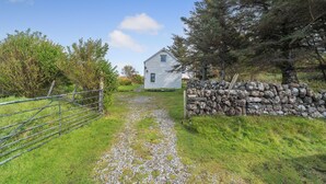 Un sentier rural mène à une maison en pierre blanche, dont un des côtés est bordé d’un mur de pierres.