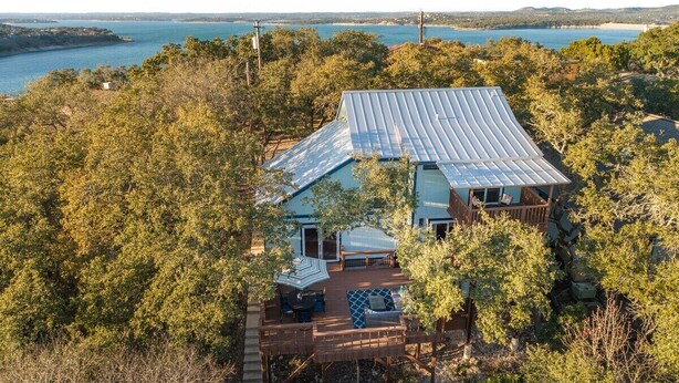 Une maison avec un toit en métal, entourée d’une forêt dense et offrant une vue sur une vaste étendue d’eau.