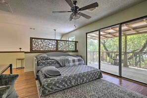 Ein Schlafzimmer mit einem Bett, einem Deckenventilator, einem großen Fenster und Blick auf Bäume.
