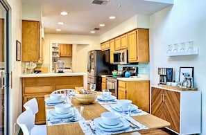 A modern kitchen with wooden cabinets, a dining table set for four, and a refrigerator.