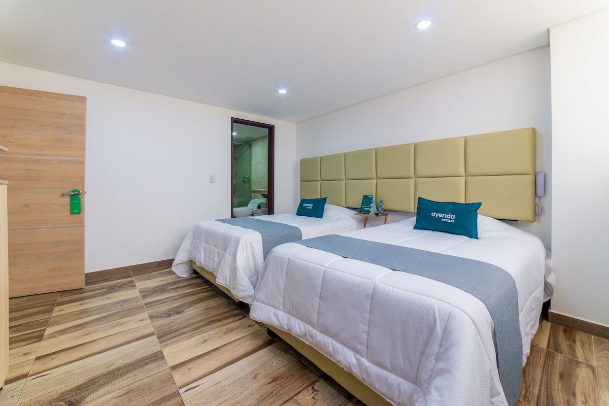 A hotel room with two beds, wooden flooring, and a modern headboard.