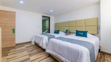 A hotel room with two beds, wooden flooring, and a modern headboard.