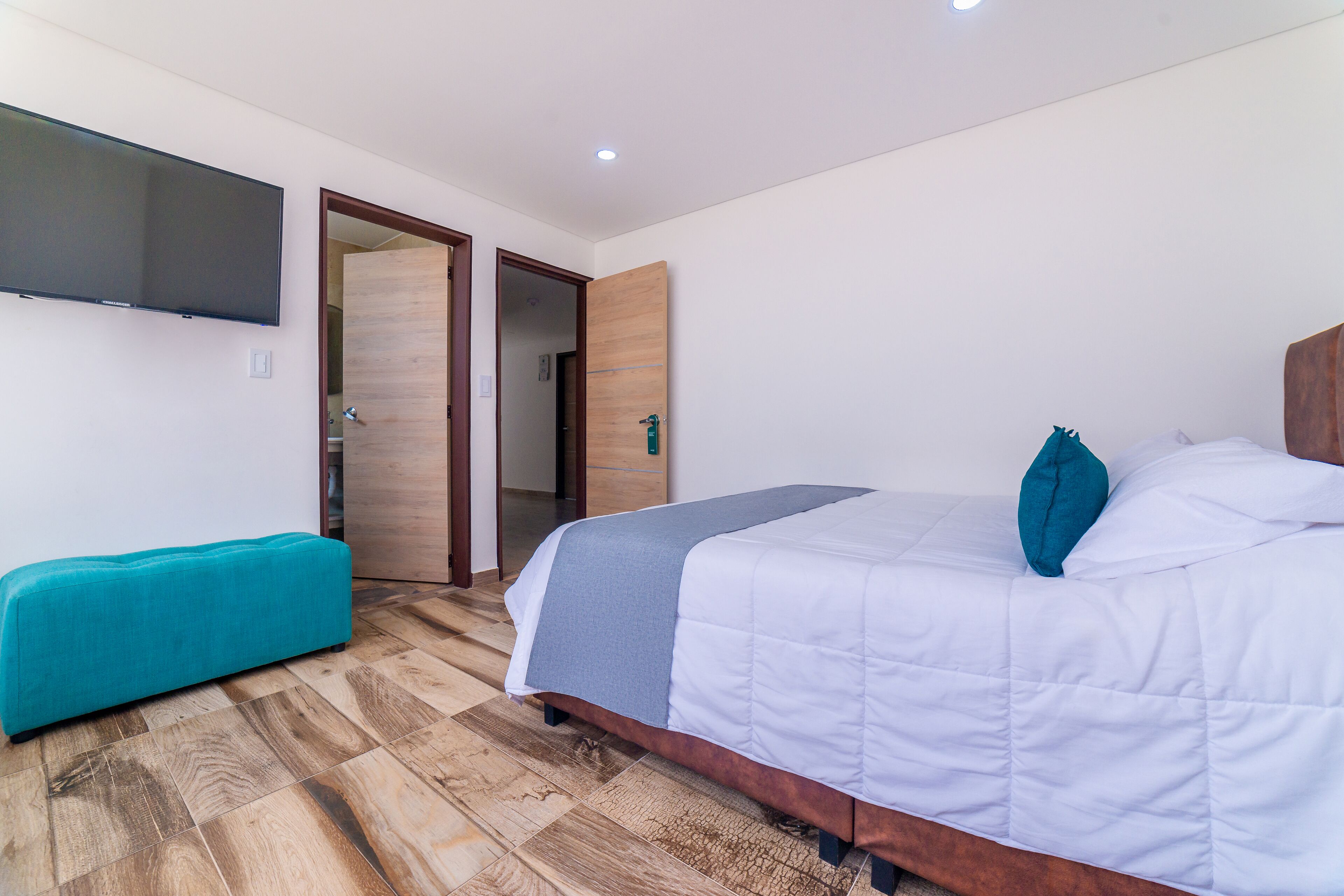 A bedroom with a bed, a bench, a TV, and a wooden door.