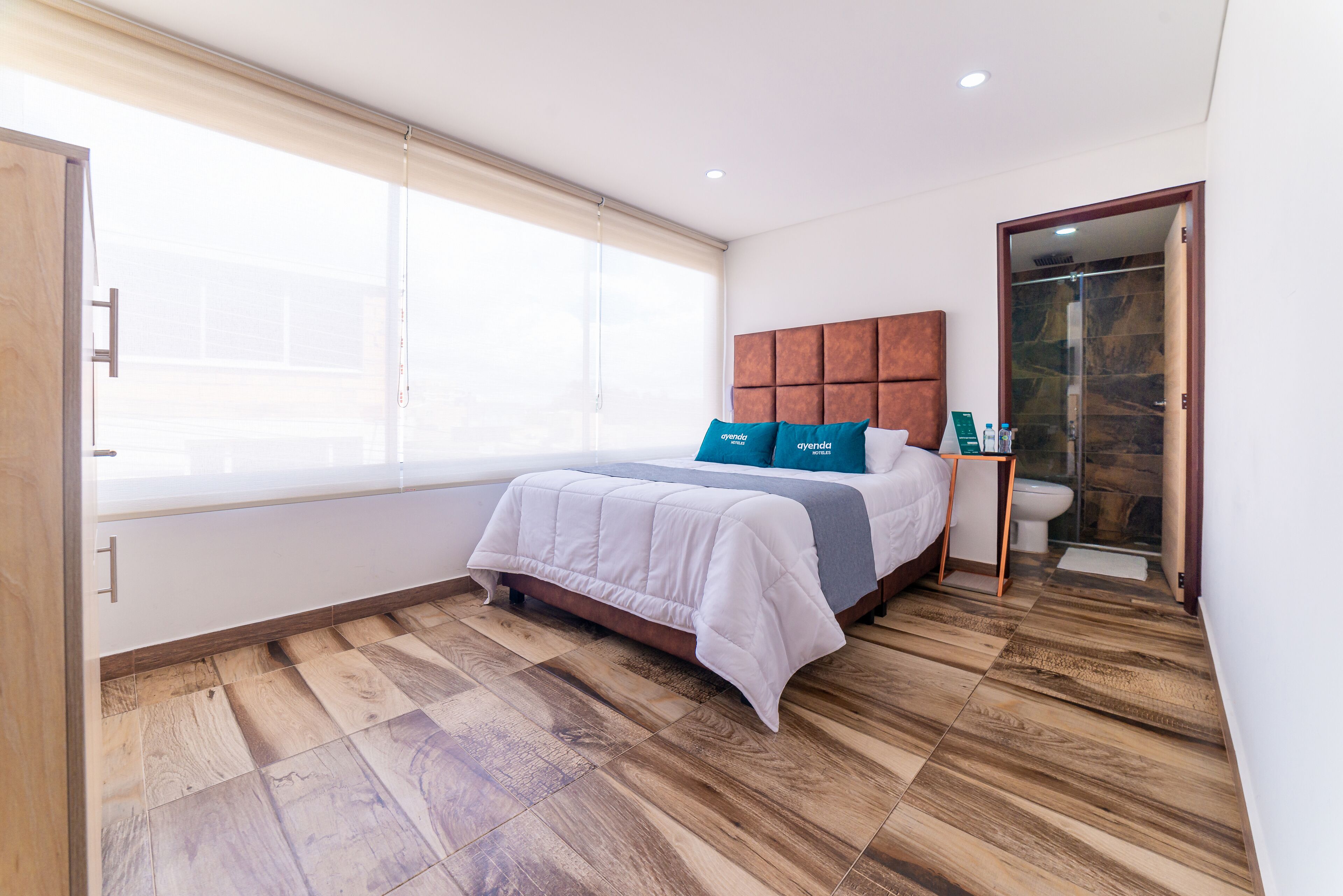 Une chambre d’hôtel moderne dotée d’un grand lit, d’un parquet, d’une salle de bain avec une douche en verre et offrant une vue sur la ville.