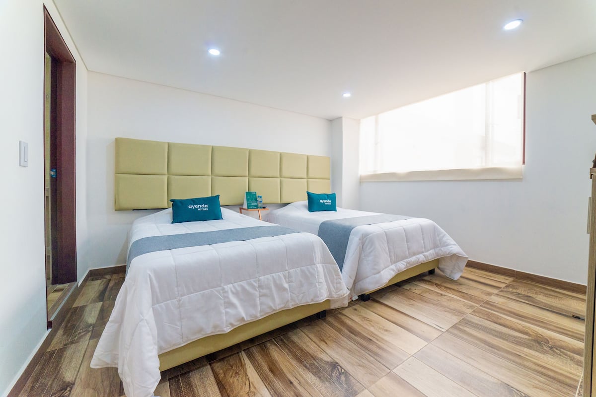 A hotel room with two beds, a wooden floor, a large window, and a modern headboard.