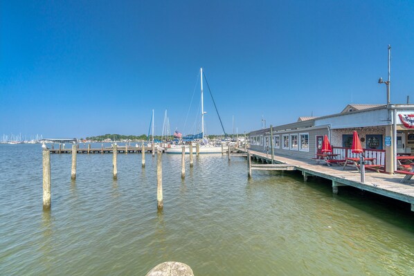 A waterfront dock with boats, a pier with red umbrellas, and a building with a flag.